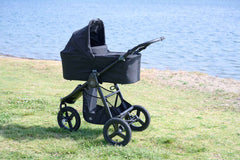 Bumbleride Single Bassinet in Black attached on Bumbleride Indie All Terrain Stroller in Black on grass near water . Global