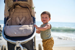 Picture of baby boy holding onto Indie All Terrain stroller frame while at the beach with ocean in background. New Collection 2022 - Global.